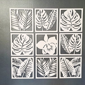May include: Nine white square wall decor pieces with cut-out tropical leaf designs. The designs include palm leaves, monstera leaves, and an orchid flower.