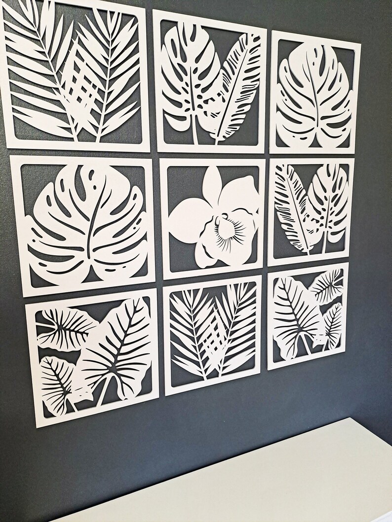 May include: Nine white wall decor pieces with a tropical leaf design. The pieces are arranged in a grid pattern on a dark gray wall.