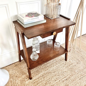 Könnte beinhalten: Eine weiße Keramik-Tasse mit schwarzem Henkel und dem Text "But First, Coffee" in fetter, schwarzer Schrift. Die Tasse steht vor einem verschwommenen Hintergrund, der eine gemütliche Umgebung suggeriert.