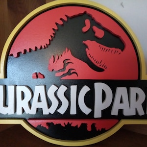 Op de afbeelding: Een houten bord met een rood en zwart Jurassic Park logo. Het logo toont een dinosaurus silhouet met de woorden "Jurassic Park" in witte letters.