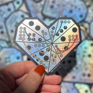 Puede incluir: Una pegatina holográfica en forma de corazón con un diseño de placa de circuito y líneas de colores. La pegatina tiene el texto "glassprints" en la esquina inferior derecha.