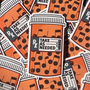 May include: A close-up of several orange pill bottle stickers with the text "Take as needed" and musical notes inside. The stickers are printed on white paper.