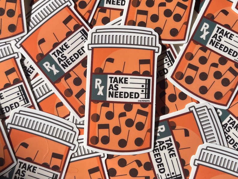 May include: A close-up of several orange pill bottle stickers with the text "Take as needed" and musical notes inside. The stickers are printed on white paper.