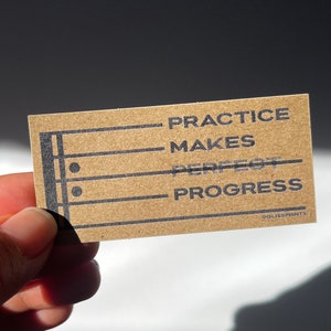May include: A brown card with black lines and text that reads "Practice Makes Perfect Progress" with a copyright symbol and "OLISS PRINTS" at the bottom.