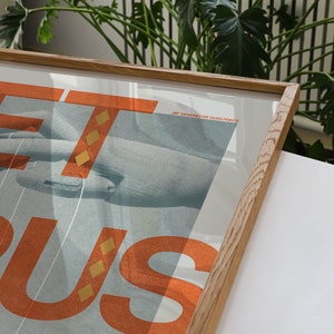 May include: A framed poster featuring the word "GET" in large orange letters with a gold pattern. The word "BUS" is in smaller orange letters with a gold pattern. The poster has a blue background with a hand reaching out from the left side of the poster. The poster has the text "Art designed by GLOSS PRINTS" in the top right corner.
