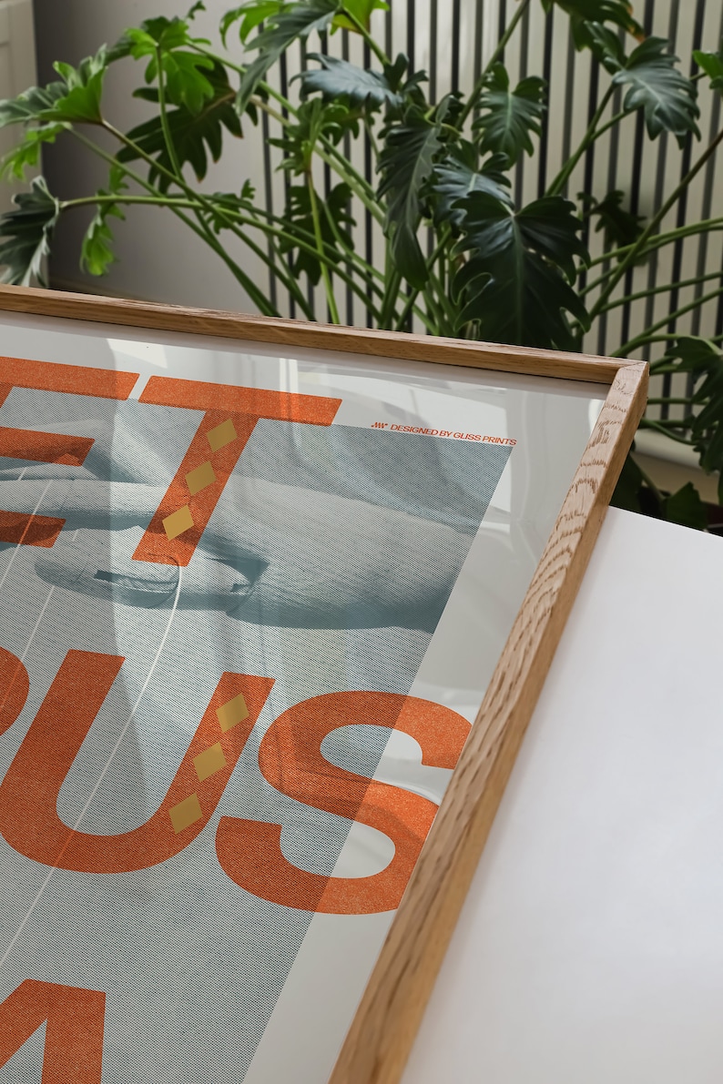 May include: A framed poster featuring the word "GET" in large orange letters with a gold pattern. The word "BUS" is in smaller orange letters with a gold pattern. The poster has a blue background with a hand reaching out from the left side of the poster. The poster has the text "Art designed by GLOSS PRINTS" in the top right corner.