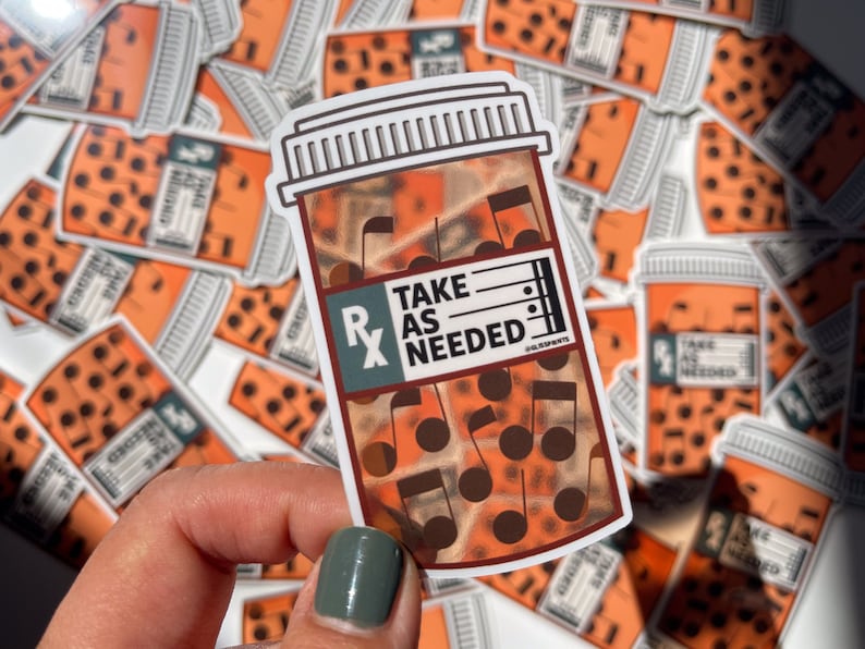 May include: A sticker of a pill bottle with musical notes inside. The bottle is orange and brown with the text "TAKE AS NEEDED" on the label.