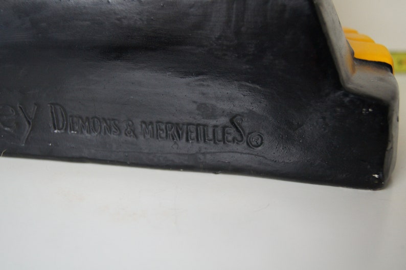 May include: Black and yellow Halloween decoration with the text "By Demons & Merveilles" on the bottom.