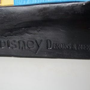 May include: Close-up of a black base with the text "&copy; Disney Demons & Merveilles" embossed on it.