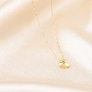 May include: A gold-colored heart pendant necklace. The heart-shaped charm is smooth and rounded, suspended from a delicate chain. The necklace is displayed on a cream-colored satin fabric.