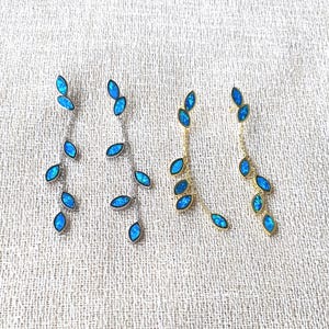 Op de afbeelding: Vier paar bungeloorbellen met een bladvormgeving. De oorbellen hebben blauwe, op opaal lijkende stenen, gezet in zilver- en goudkleurig metaal. De bladeren zijn in een trapsgewijs patroon gerangschikt, wat een elegante en delicate uitstraling creëert.