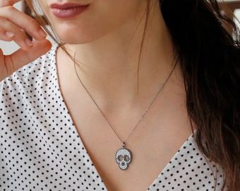 Puede incluir: Un collar de cadena de plata con un colgante de calavera. La calavera está hecha de metal negro y está cubierta de pequeñas piedras blancas.