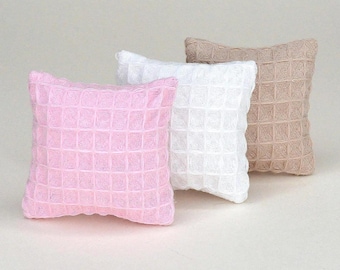 May include: Three square throw pillows arranged in a row, featuring a textured waffle-knit pattern. The pillows are coloured in light pink, white, and beige, each displaying a consistent grid-like fabric structure across the entire surface area.