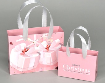 May include: Two pink gift bags with white satin handles. The larger bag has a design of presents with pink bows and gold glitter. The smaller bag has the text "Merry Christmas and Happy New Year".