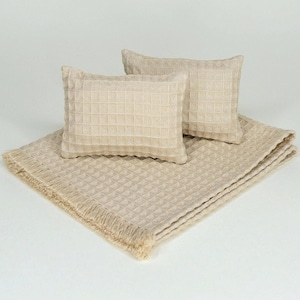 May include: A beige waffle-textured throw blanket with fringed edges paired with two matching rectangular throw pillows. The set features a consistent grid pattern across all items, showcasing a uniform light tan color and a soft, woven fabric.