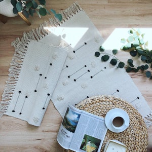 May include: Two white woven rugs with black dots and fringe edges. The rugs are layered on top of each other. A magazine with the text "HISTORY THROUGH ART" is on top of the rugs. A woven wicker basket is in the background.