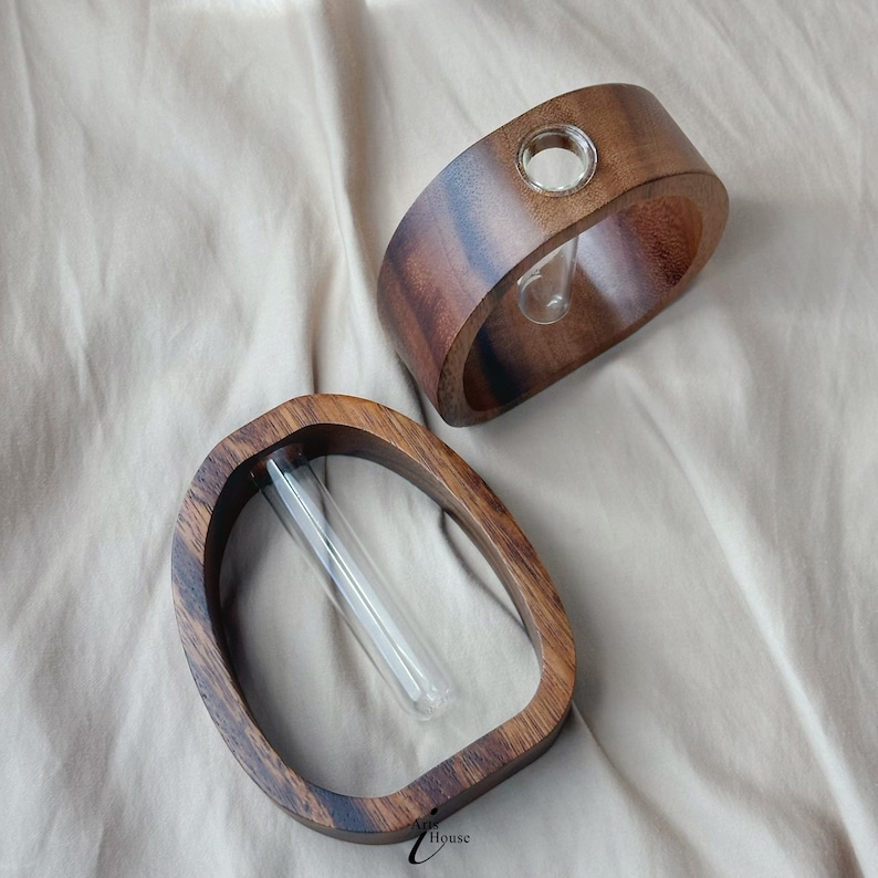 May include: Two wooden vases with glass tubes for holding flowers. The vases are both oval shaped and have a dark brown wood grain.