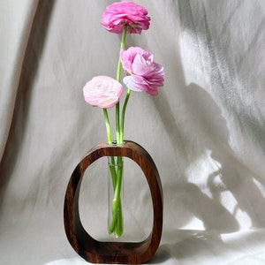 May include: A wooden vase with a round opening, holding a bouquet of pink ranunculus flowers.
