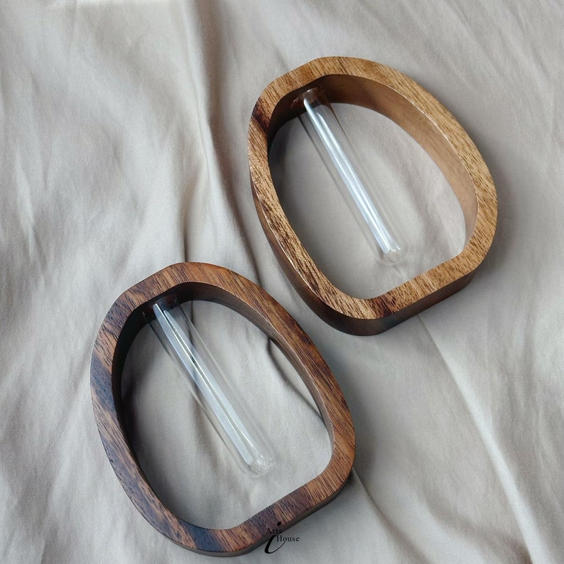 May include: Two wooden vases with a rounded shape and a clear glass tube insert. The vases are made of dark wood with a natural finish.