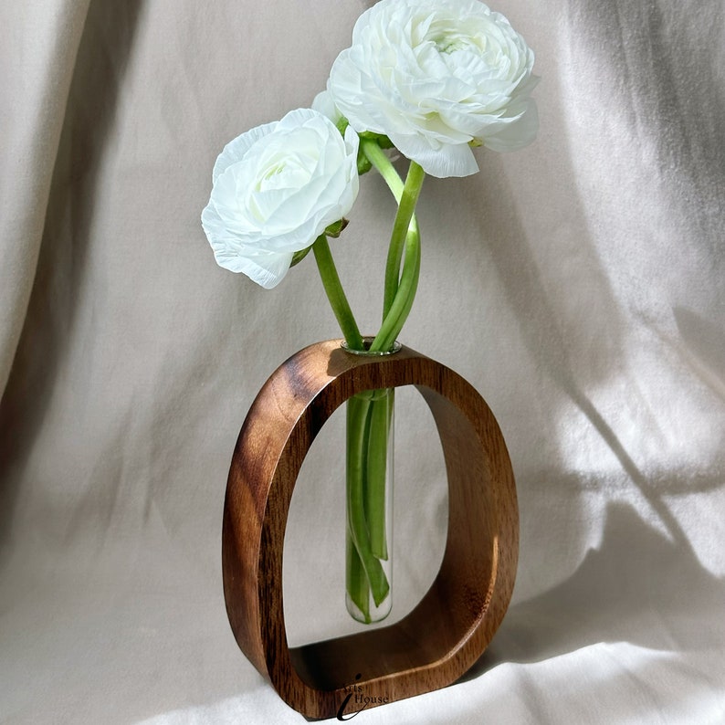 May include: A wooden vase with a circular opening holds a bouquet of three white ranunculus flowers.