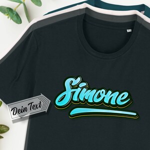 Könnte beinhalten: Ein dunkelblaues T-Shirt mit dem Wort "Simone" in einer stilisierten blauen und gelben Schrift. Der Text befindet sich auf einem schwarzen und gelben Streifen. Der Text "Dein Text" befindet sich auf einem weißen Etikett.