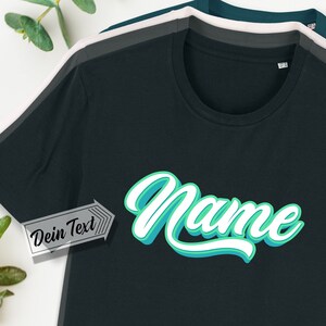 Könnte beinhalten: Ein schwarzes T-Shirt mit einer türkisfarbenen und weißen Grafik, auf der in einer Retro-Schrift "Name" steht. Der Text "Dein Text" ist in einem weißen Kasten mit schwarzem Rand sichtbar.