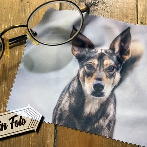 May include: A white microfiber cleaning cloth with a printed image of a dog's face. The dog has brown, black, and grey fur. The text "Dein Foto" is printed on a brown tag in the bottom left corner of the image.