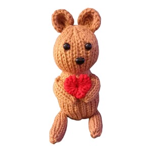 May include: A brown knitted stuffed animal holding a red heart. The animal has a black nose and black eyes.