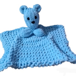 May include: A light blue baby comforter featuring a bear's head and small arms. The bear has black eyes and a black nose. The square blanket has a textured, looped design and a ruffled edge. The toy is made of soft, plush material.