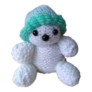May include: A white crocheted teddy bear wearing a light blue and green crocheted hat.