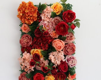 May include: A rectangular floral arrangement featuring a variety of roses and hydrangeas in shades of red, orange, yellow, and pink. The flowers are set against a backdrop of green foliage, creating a vibrant and textured display.