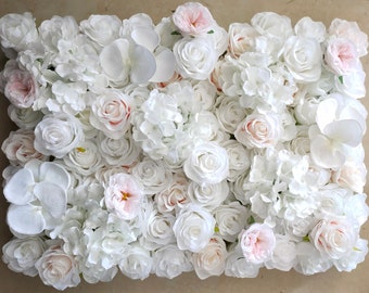 May include: A white and blush artificial flower wall with a variety of flowers, including roses, hydrangeas, and orchids.