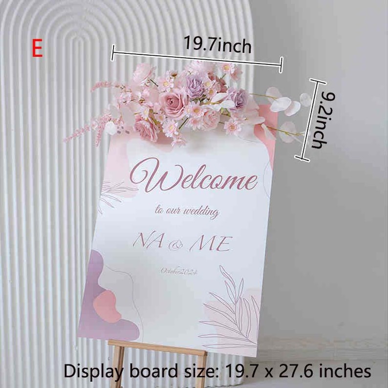 May include: A wedding welcome sign with the text "Welcome to our wedding NA & ME October 2024". The sign is decorated with pink and purple flowers and measures 19.7 x 27.6 inches. The sign is supported by a wooden easel.