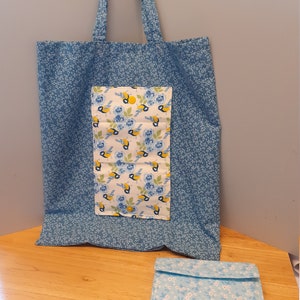 May include: A blue tote bag with a smaller blue pocket featuring a white background with a pattern of yellow birds and blue flowers. A smaller blue bag with a white floral pattern is also pictured.