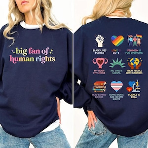 Könnte beinhalten: Marineblaues Sweatshirt mit dem Schriftzug "big fan of human rights" in bunten Buchstaben. Auf der Rückseite befinden sich verschiedene Grafiken und Slogans, darunter "Black Lives Matter" und "Love is Love."
