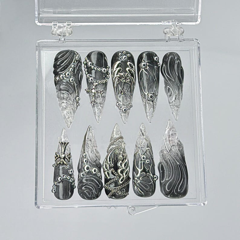 Puede incluir: Una caja de pl&aacute;stico transparente con 10 u&ntilde;as postizas. Las u&ntilde;as son negras con detalles y dise&ntilde;os plateados. Las u&ntilde;as est&aacute;n dispuestas en dos filas de cinco.