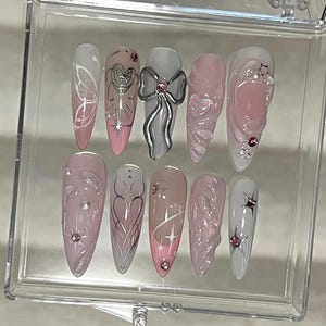 May include: A set of ten false nails with different designs. The nails are all a light pink color with white and silver accents. Some of the designs include butterflies, hearts, and bows.