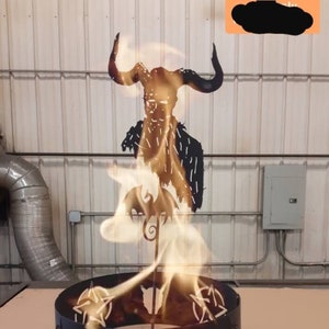 May include: A black metal fire pit with a pentagram design and a bull's head silhouette. The fire pit is topped with a metal sculpture of a horned figure with flames rising from the top.