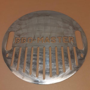 K&ouml;nnte beinhalten: Ein runder, silberner Grillrost aus Metall mit den ausgeschnittenen Worten "BBQ-MASTER". Der Rost hat eine Reihe von vertikalen Schlitzen, die hineingeschnitten sind.