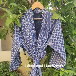 May include: A blue and white cotton kimono robe with a patchwork design. The robe has a tie belt and long sleeves. The text "Dhanlaxmi Handicraft" is visible on the robe.