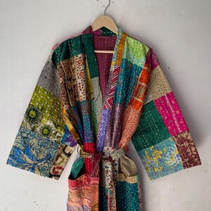 May include: A patchwork robe with a vibrant mix of colors and patterns. The robe features a belt and pockets, and is displayed on a wooden hanger. The design incorporates various fabrics and textures, creating a unique and artistic look.