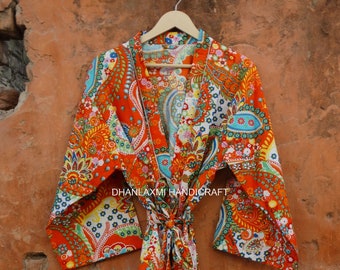May include: A bright orange robe featuring a multi-colored floral and paisley pattern with blue, yellow, and green accents. The garment has wide sleeves, a tie-waist belt, and the text DHANLAXMI HANDICRAFT printed across the center front.