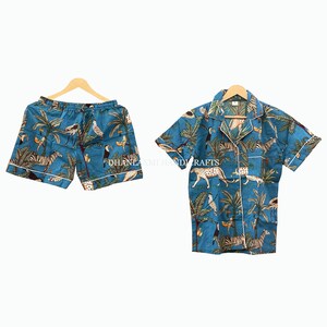 Puede incluir: Un conjunto de pijama azul con una camisa de manga corta y pantalones cortos. La camisa y los pantalones cortos tienen un estampado tropical con palmeras, cebras y pájaros.