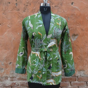 May include: A green quilted jacket with a floral and animal print. The jacket has a tie belt and long sleeves.