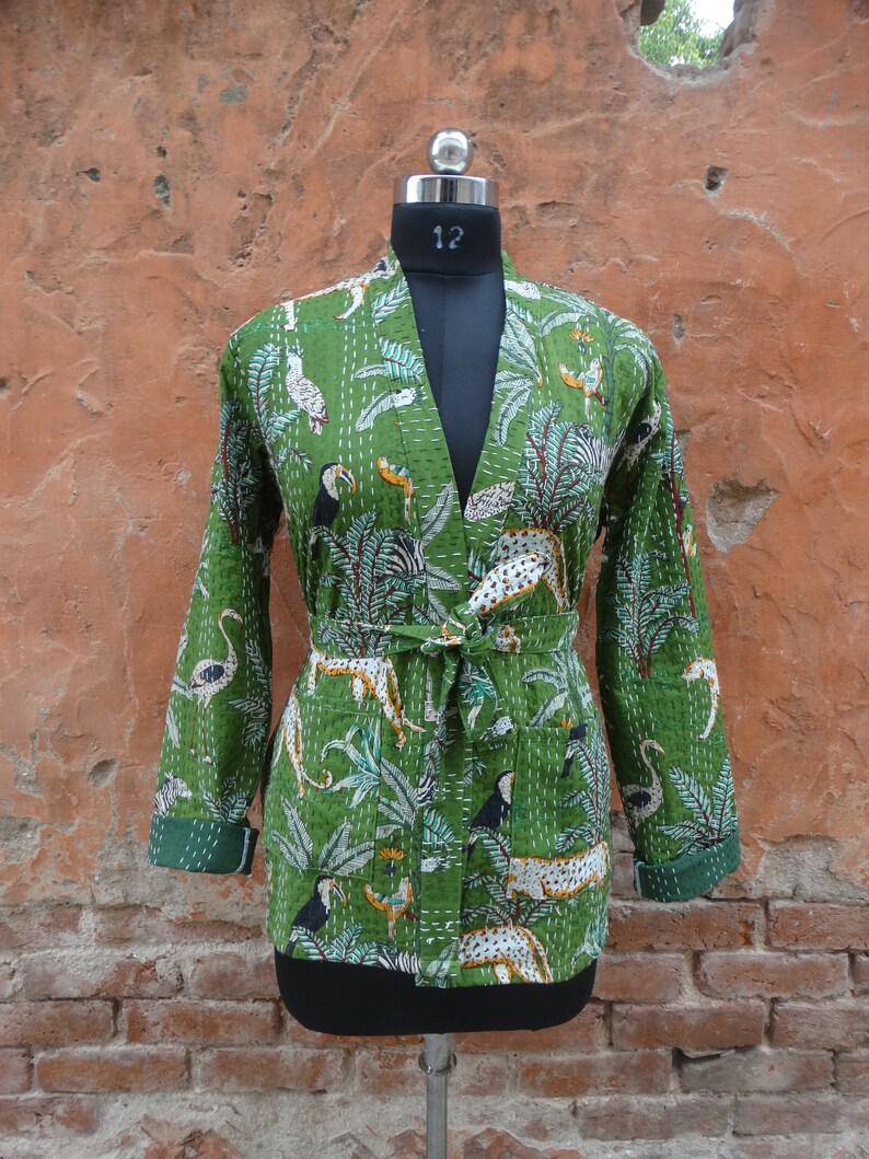May include: A green quilted jacket with a floral and animal print. The jacket has a tie belt and long sleeves.