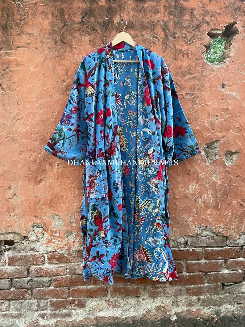 May include: A blue cotton robe with a floral and bird print. The robe has a tie belt and is open in the front. The text "DHANLAXMI HANDICRAFTS" is printed on the bottom of the robe.