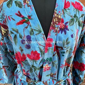May include: A blue velvet robe with a floral and bird print. The robe has a tie belt and long sleeves. The text "DHANLAXMI HANDICRAFTS" is printed on the robe.
