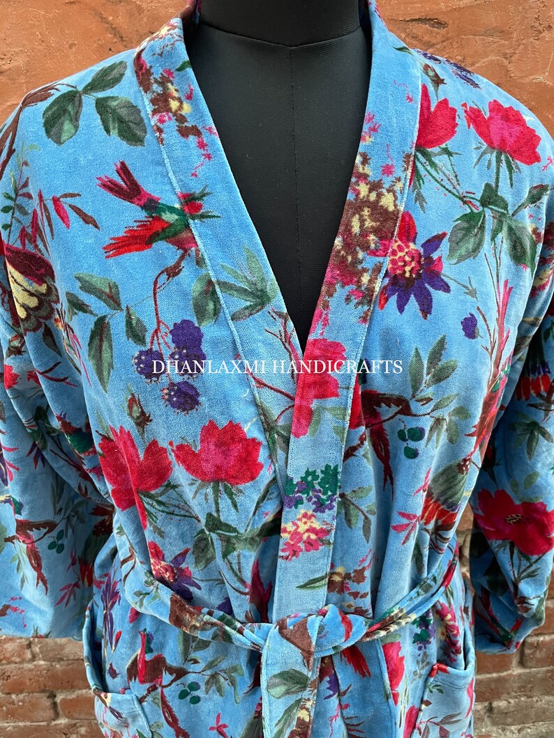 May include: A blue velvet robe with a floral and bird print. The robe has a tie belt and long sleeves. The text "DHANLAXMI HANDICRAFTS" is printed on the robe.