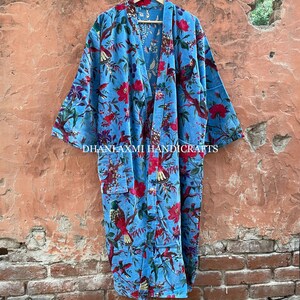 May include: A blue cotton robe with a floral and bird print. The robe has a long, flowing silhouette and a tie closure at the front. The text "DHANLAXMI HANDICRAFTS" is printed on the bottom of the robe.