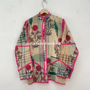 May include: A long-sleeve jacket featuring a cream-colored base with a floral pattern in red, green, and blue, accented by bright pink piping along the edges, collar, and pockets. The text "dhanlaxmihandicraft" is printed across the center.